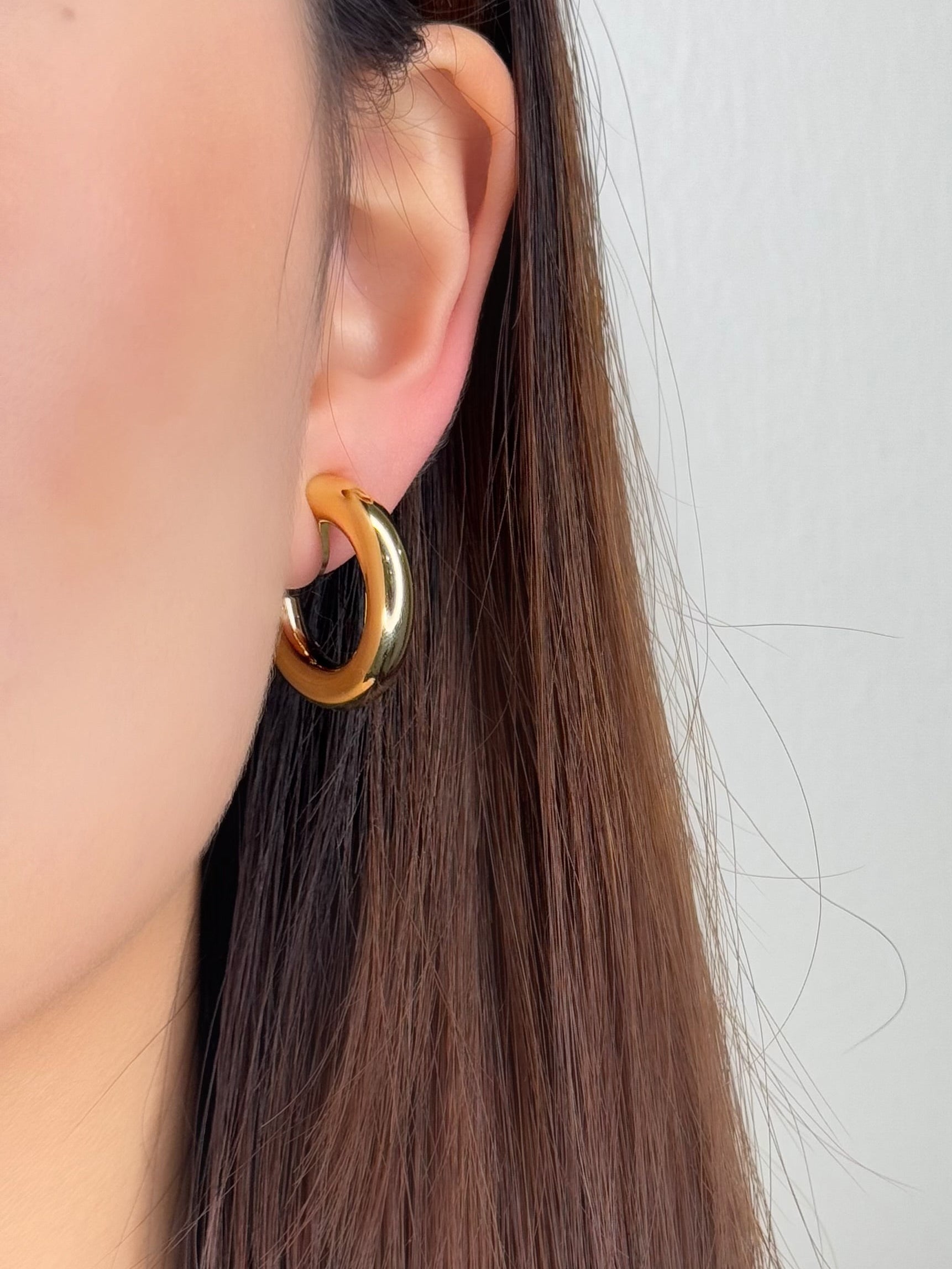Model profile view styling a chunky gold tube clip on earring flush against the earlobe