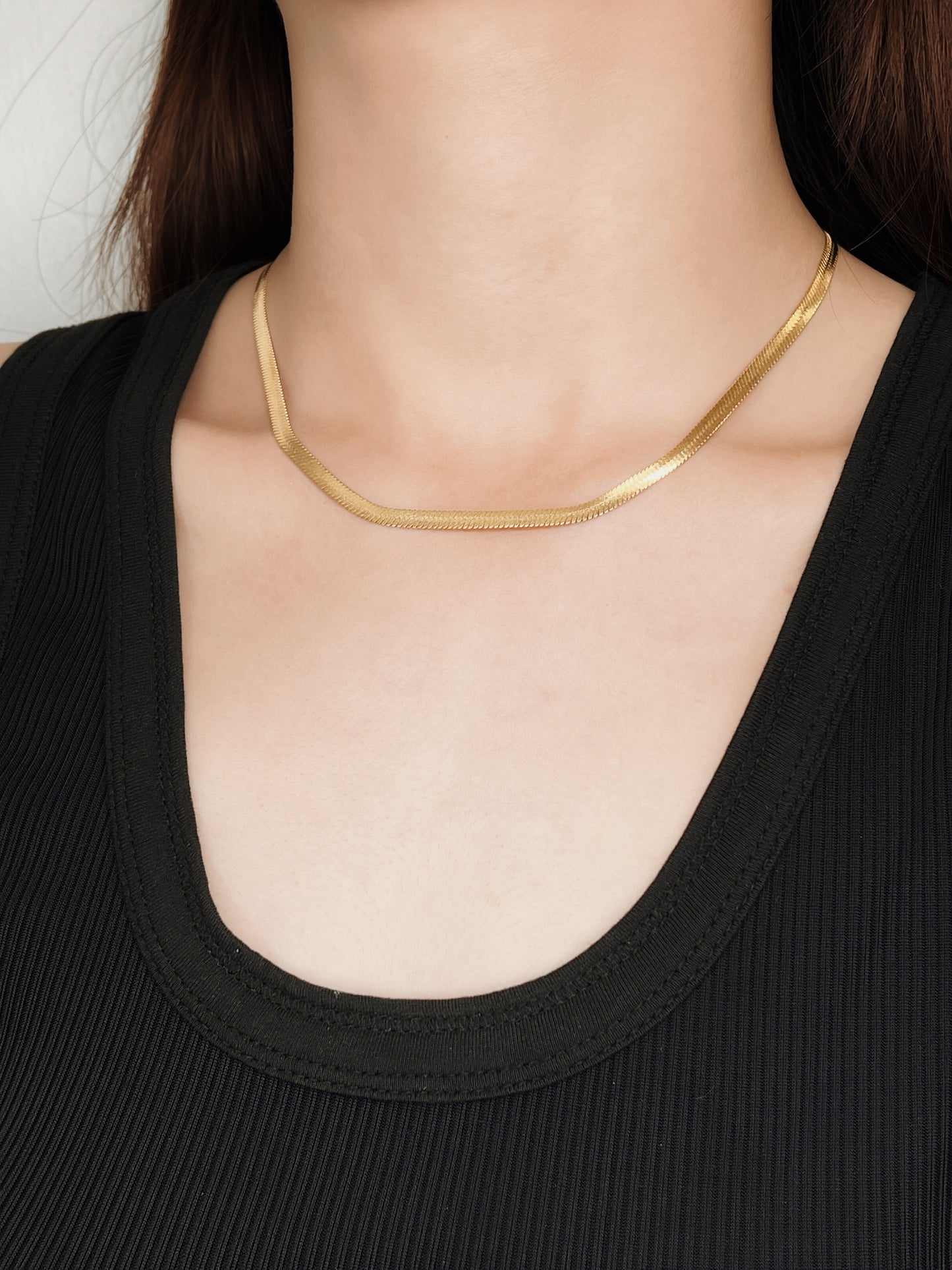 Model profile view styling gold snake chain necklaces against a black tank top