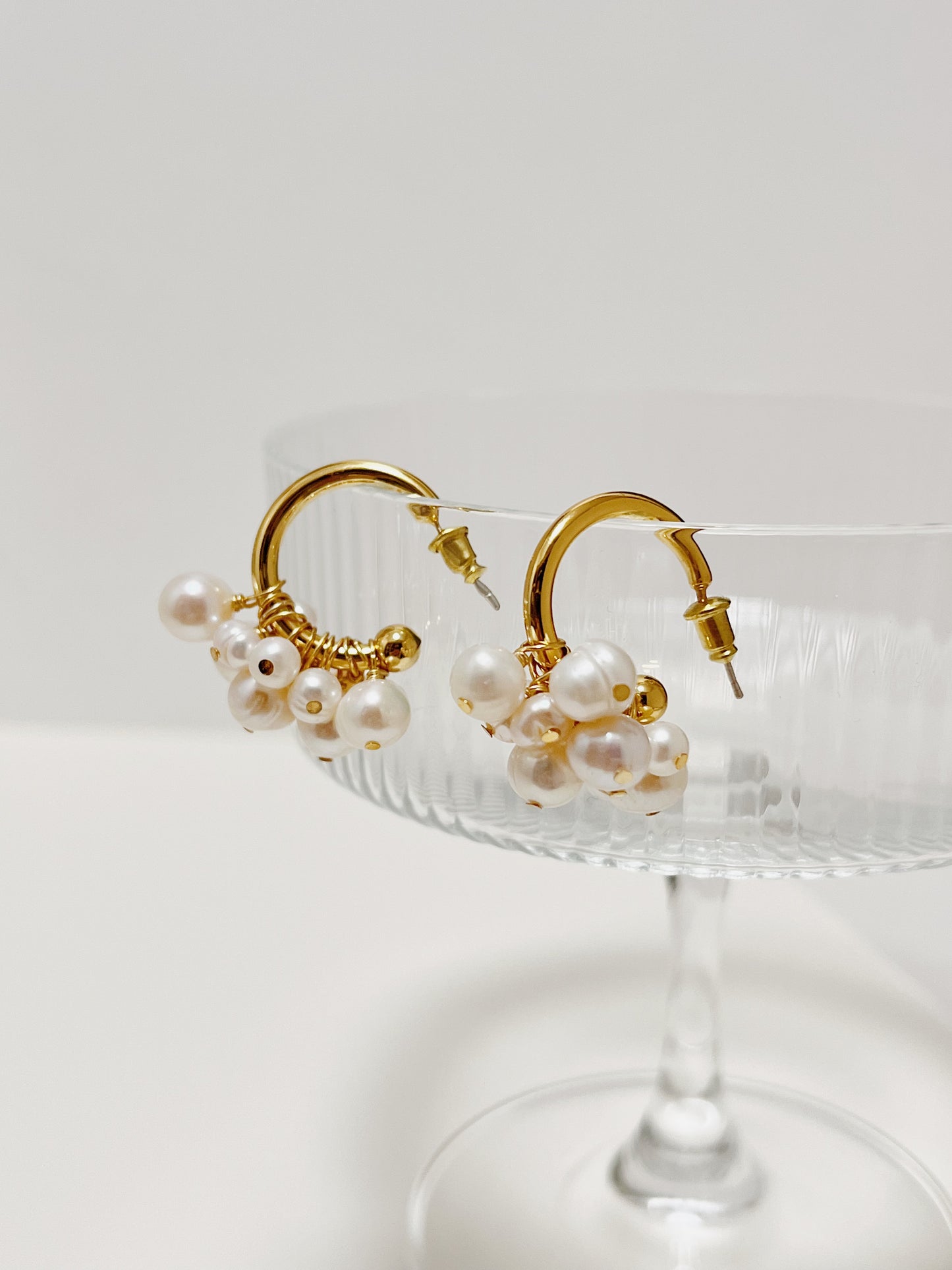 Angled overhead view of the Freya organic freshwater pearl statement earrings balancing on clear glassware to highlight how multiple pearls hug the arc.