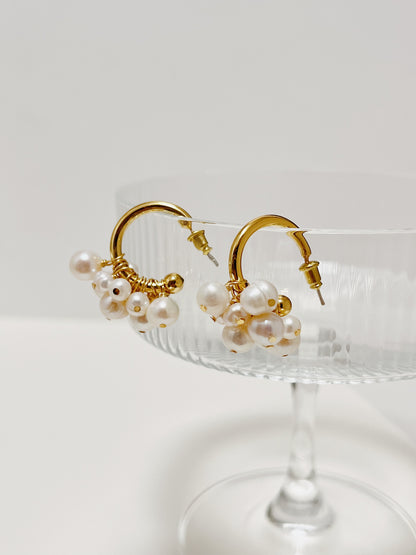 Angled overhead view of the Freya organic freshwater pearl statement earrings balancing on clear glassware to highlight how multiple pearls hug the arc.