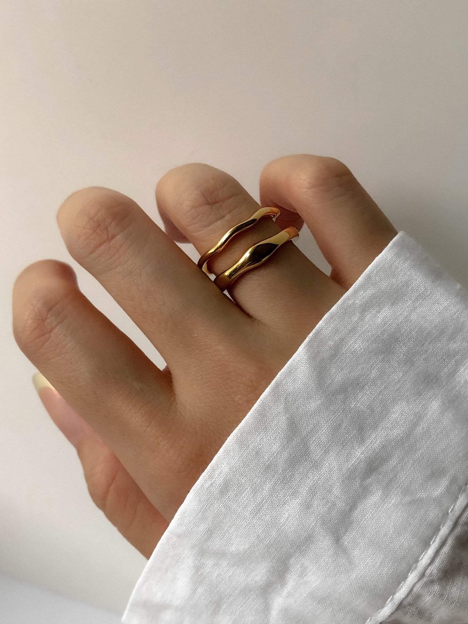 Model styled in an oversized white linen shirt wearing wavy gold bands on ring finger.
