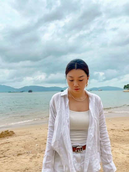 Elegant summer lifestyle view of a woman wearing a skin safe hypoallergenic small pearl necklace against a coastal backdrop