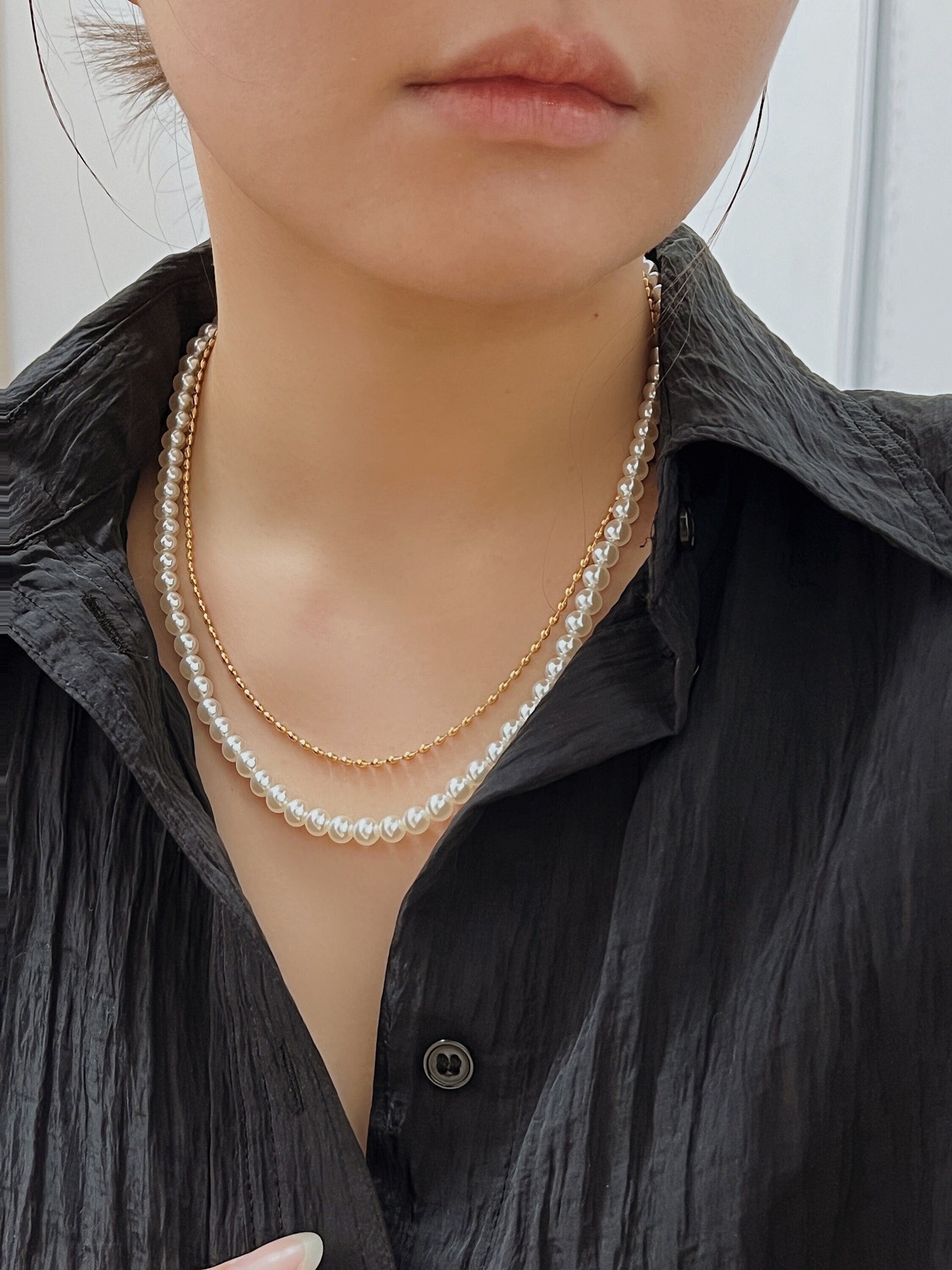 Editorial style crop pairing a micro textured gold bead chain with a natural pearl strand on a model