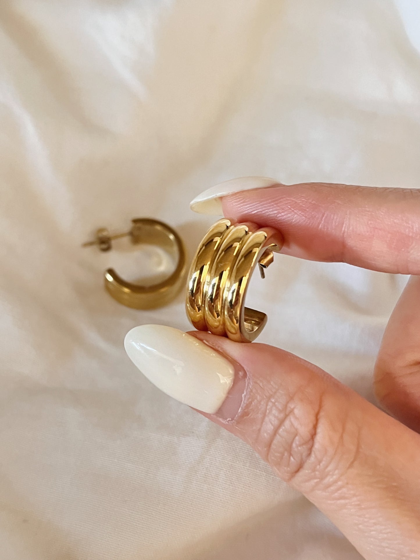 Close-up macro shot of the Lucia Ribbed Hoop Earring held between fingers, showing the flawless reflection of its warm 18K gold PVD finish.