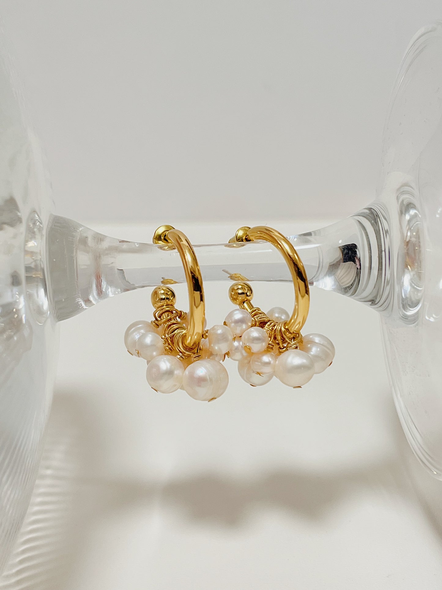 Parallel studio composition of the Freya premium pearl hoop earrings balanced on a crystal stand, emphasizing the secure closure architecture and wire loops.