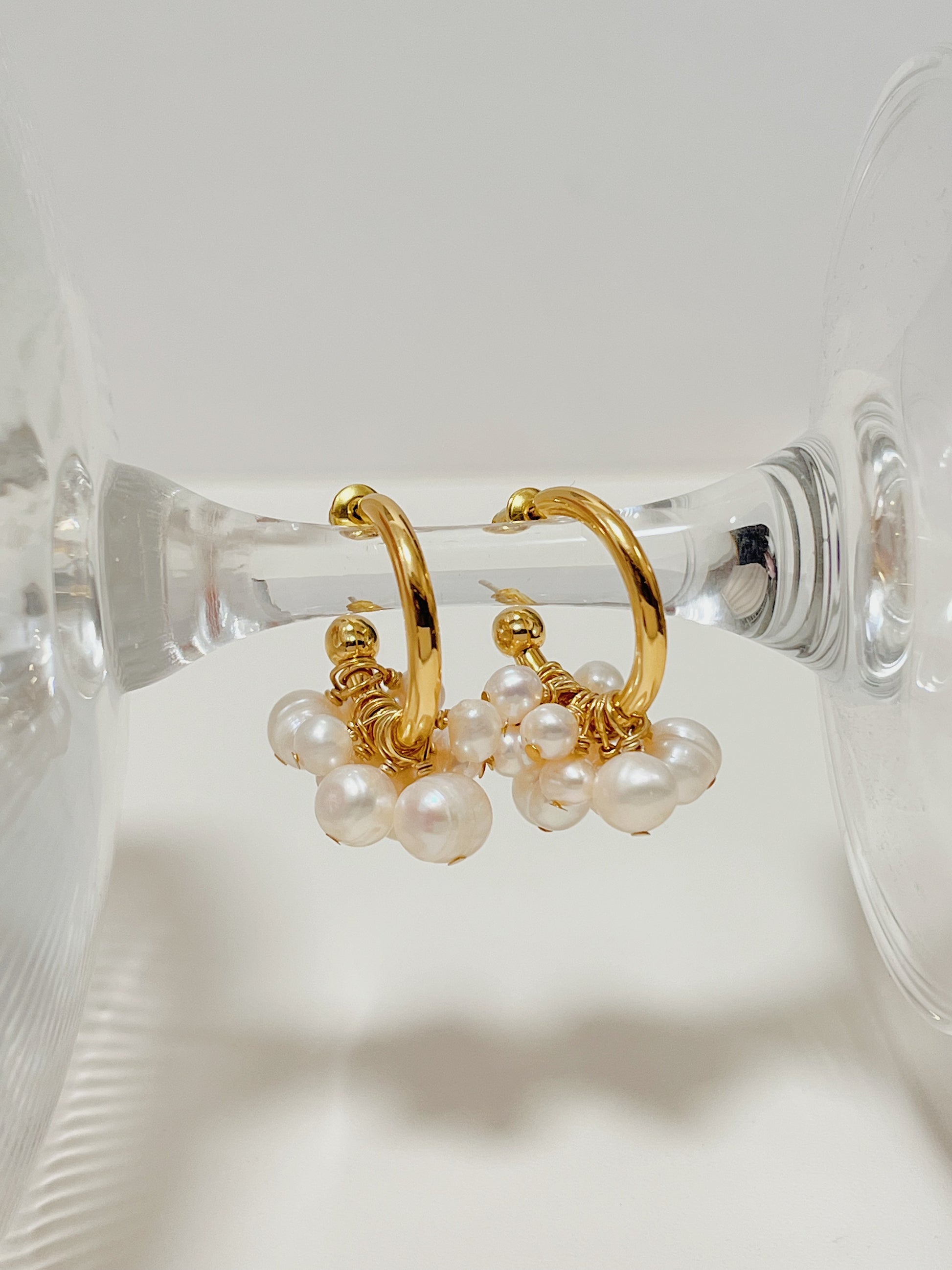 Parallel studio composition of the Freya premium pearl hoop earrings balanced on a crystal stand, emphasizing the secure closure architecture and wire loops.