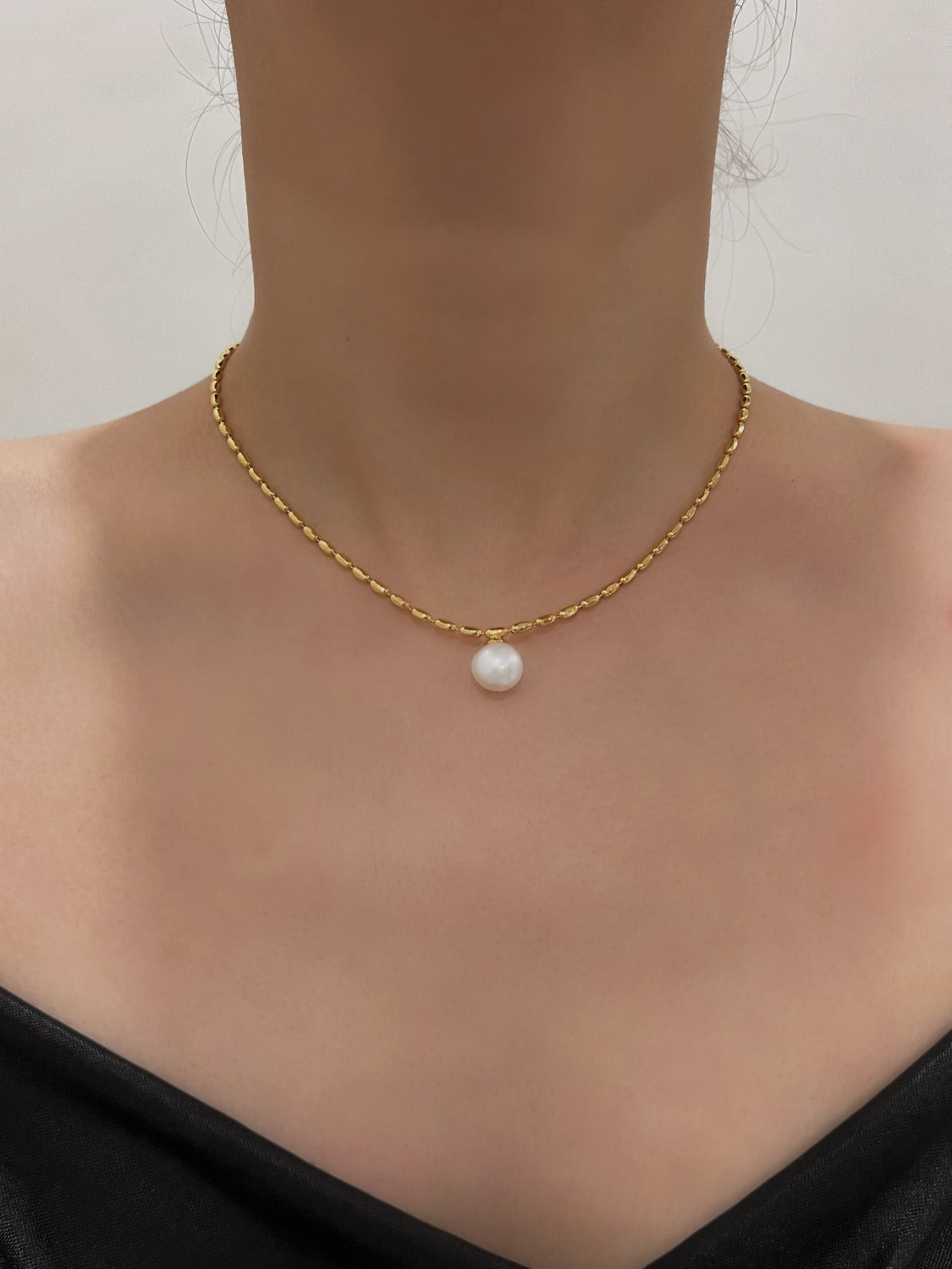 Neck profile of a woman showcasing an elegant freshwater pearl pendant choker against a clean studio backdrop
