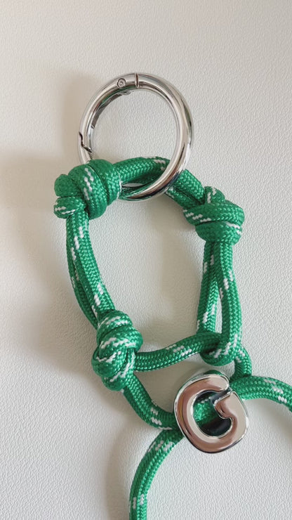Oversized chrome initial letter G bead suspended from a green and white patterned tactical cord loop