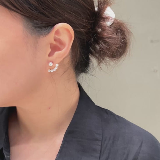 A video of a close-up look of a woman wearing a pearl ear jacket earring with a neutral background