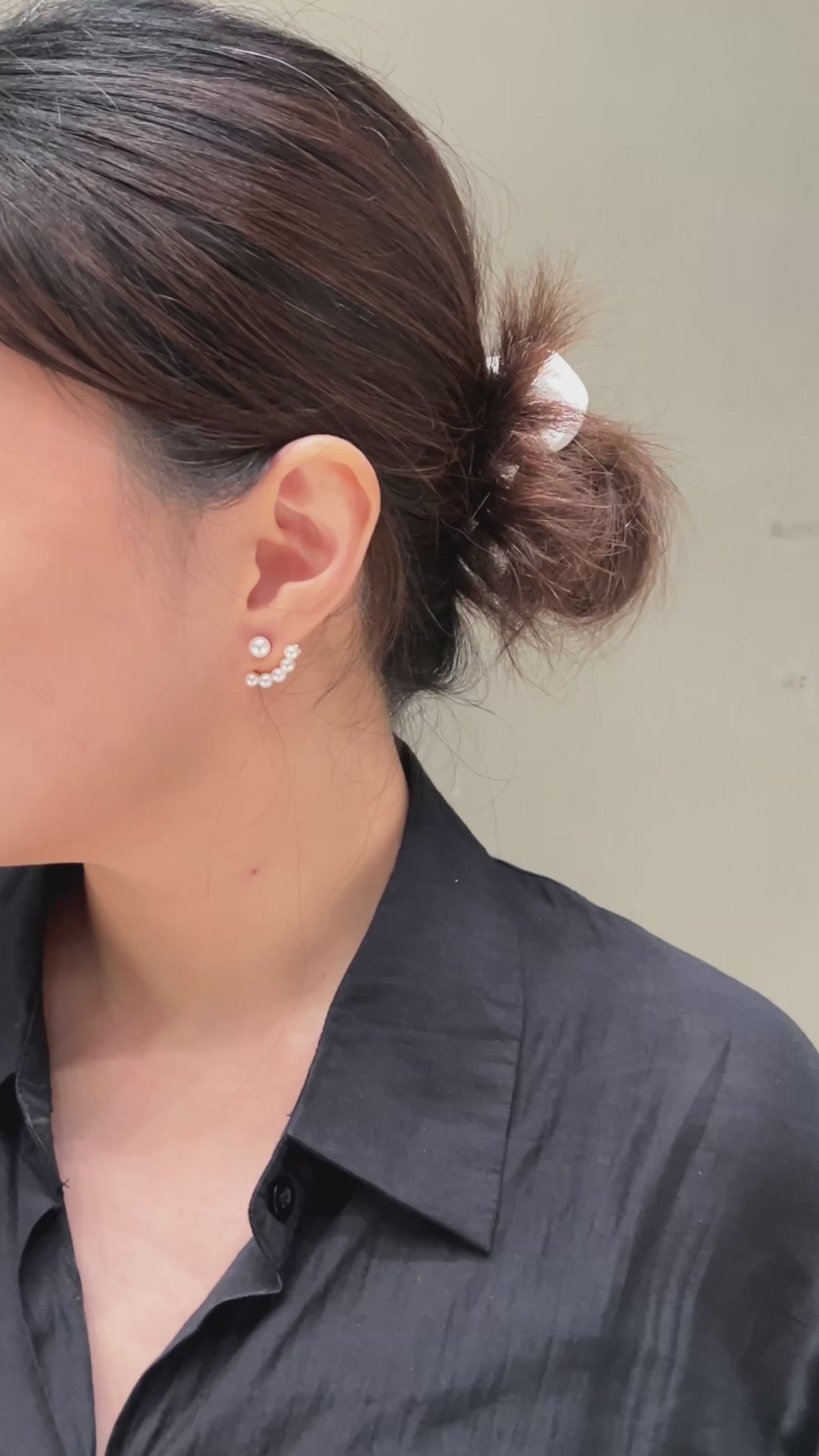 A video of a close-up look of a woman wearing a pearl ear jacket earring with a neutral background