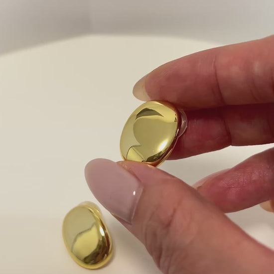 Product shot showcasing the high shine finishes, the side engraved logo and the flexible clear cushion pad attached to the adjustable spiral clip mechanism on the margaux gold oval clip on earrings by aurous atelier