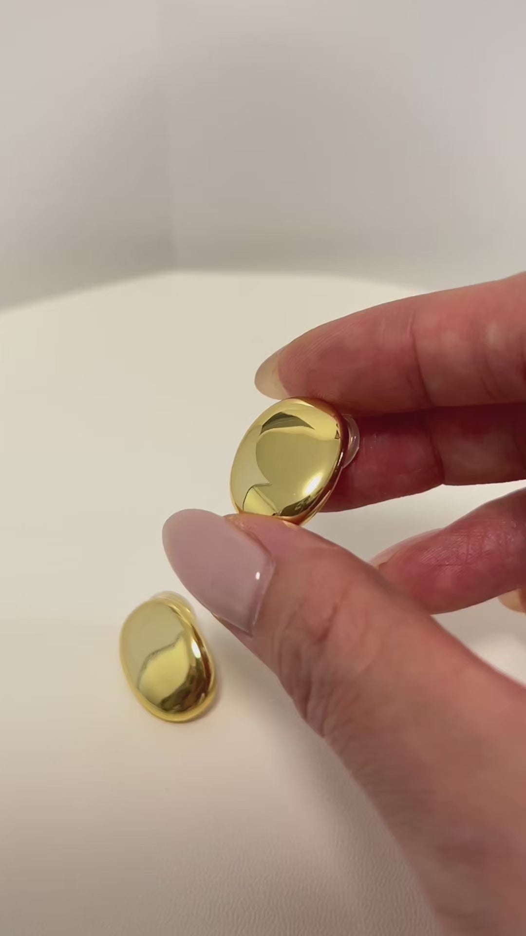 Product shot showcasing the high shine finishes, the side engraved logo and the flexible clear cushion pad attached to the adjustable spiral clip mechanism on the margaux gold oval clip on earrings by aurous atelier