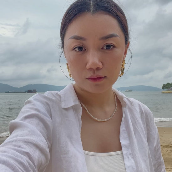 Elegant summer lifestyle view of a woman wearing a skin safe hypoallergenic small pearl necklace against a coastal backdrop