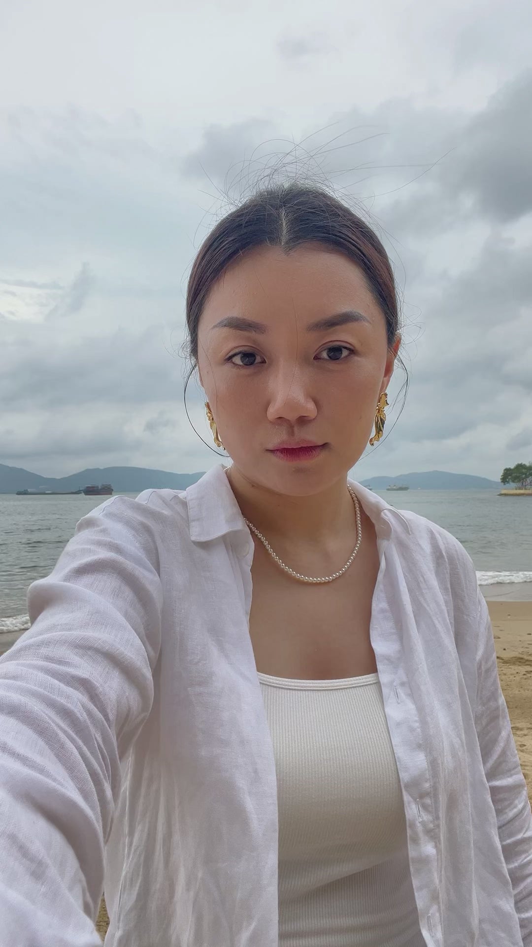 Elegant summer lifestyle view of a woman wearing a skin safe hypoallergenic small pearl necklace against a coastal backdrop