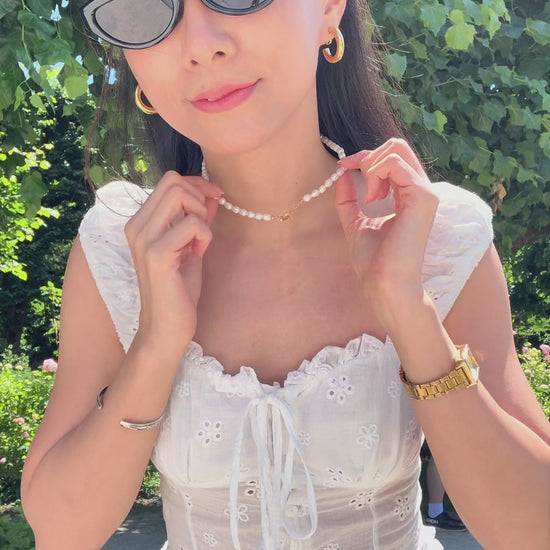 Outdoor shot of a woman styling the toggle clasp of the genuine freshwater pearl necklace on her neck and harper clip on hoops on her ear lobes with summer outfits.