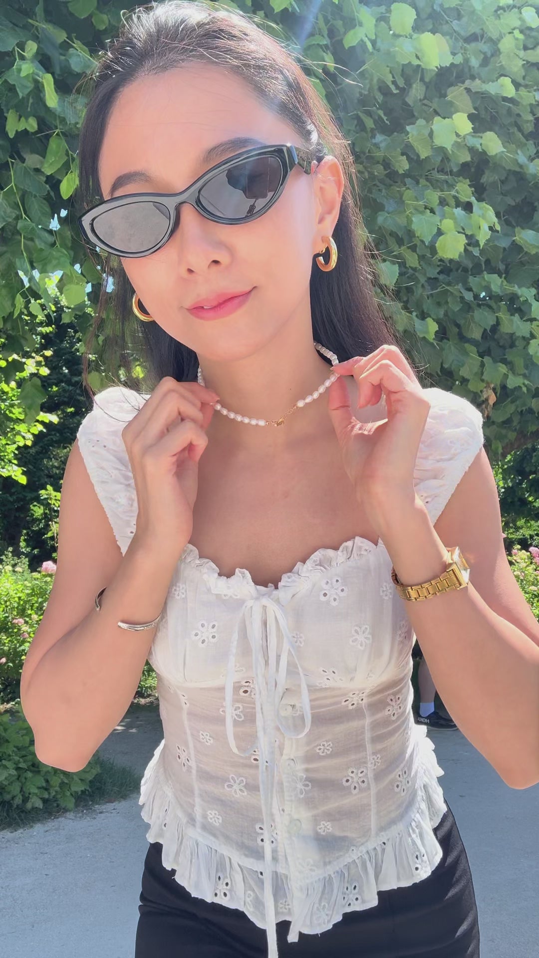 Outdoor shot of a woman styling the toggle clasp of the genuine freshwater pearl necklace on her neck and harper clip on hoops on her ear lobes with summer outfits.