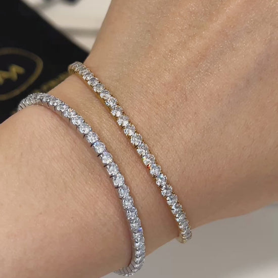 A wrist wearing a silver and gold diamond tennis bracelet with a black pouch in the background