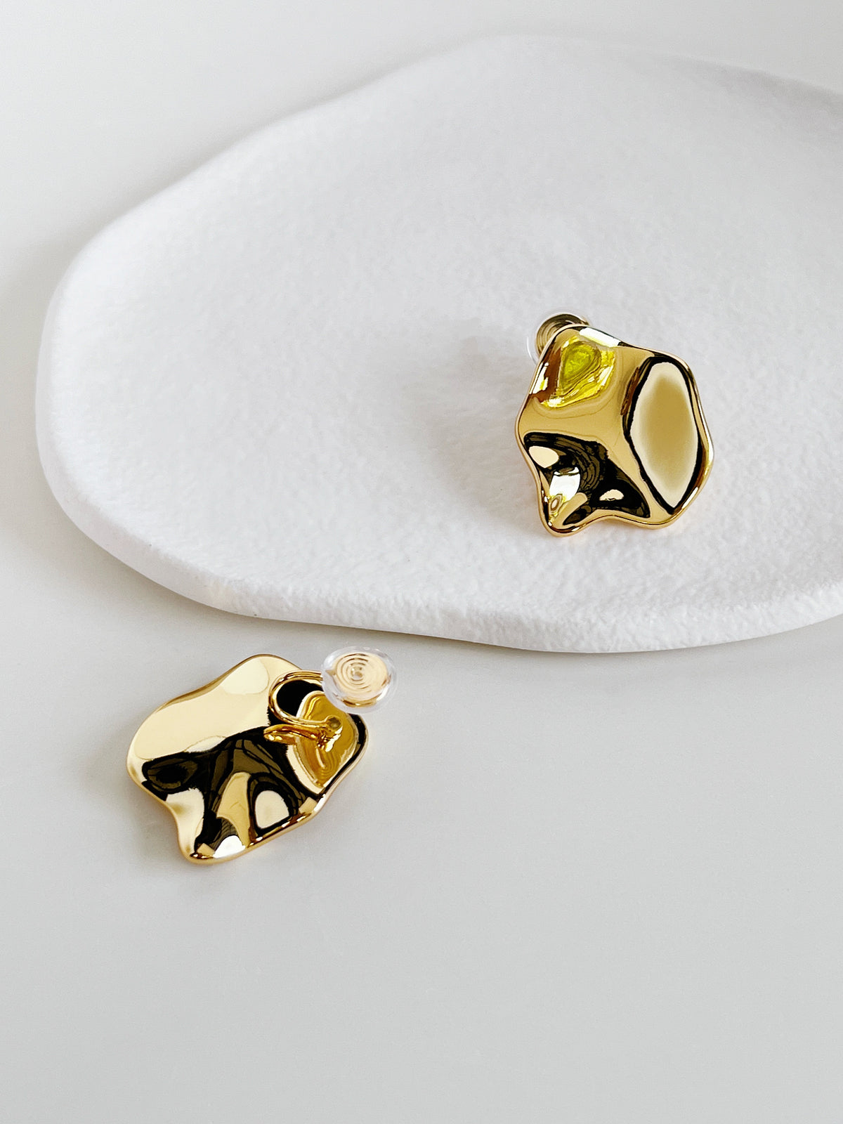 Close-up detail of the spiral coil clip-on mechanism fitted with a clear non-slip silicone pad on the hollowed reverse plate of a gold statement earring.