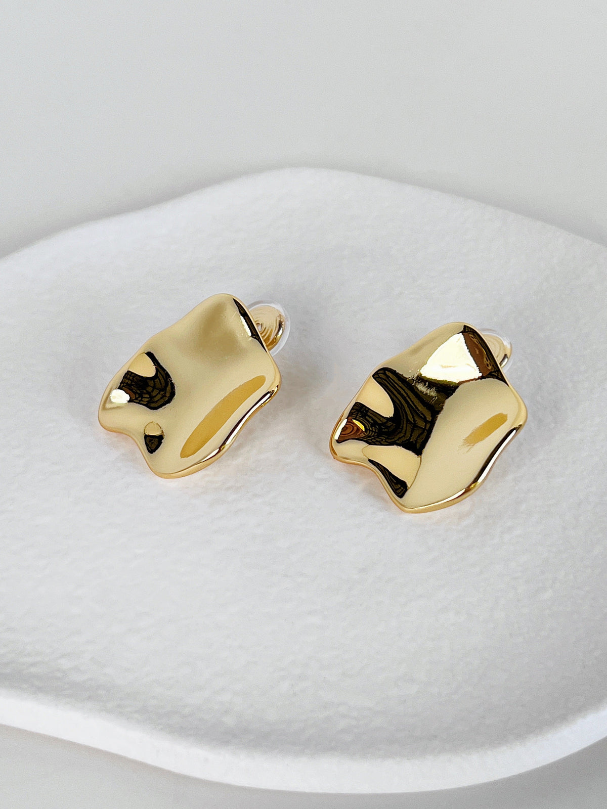 Pair of 18k gold plated 29mm crumpled statement clip-on earrings showcasing liquid mirror polish displayed on a textured white surface.