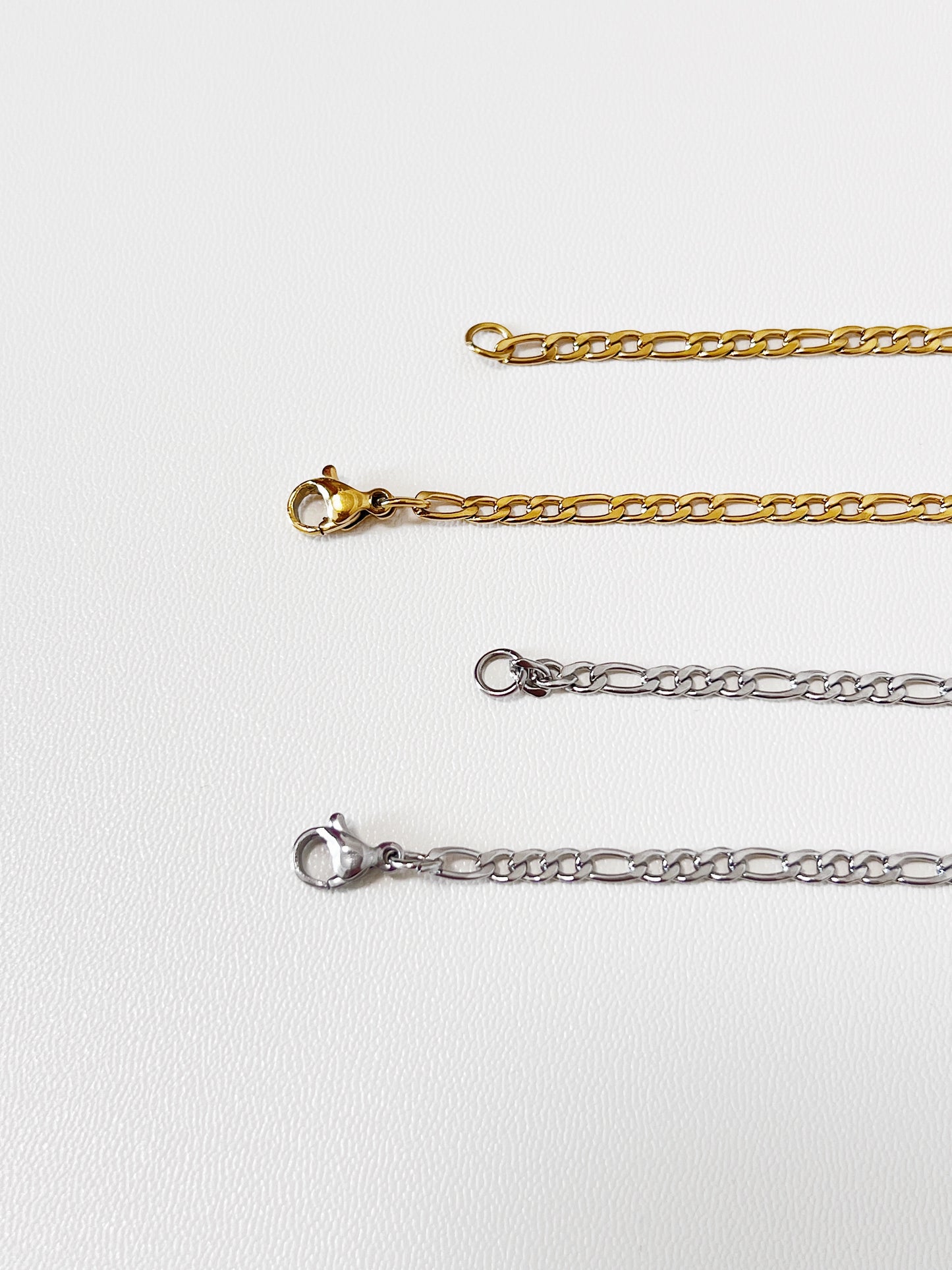 Close-up macro view of the Rhea necklace closure mechanism, focusing on the sleek gold lobster clasp and the clean lines of the silver lobster clasp.