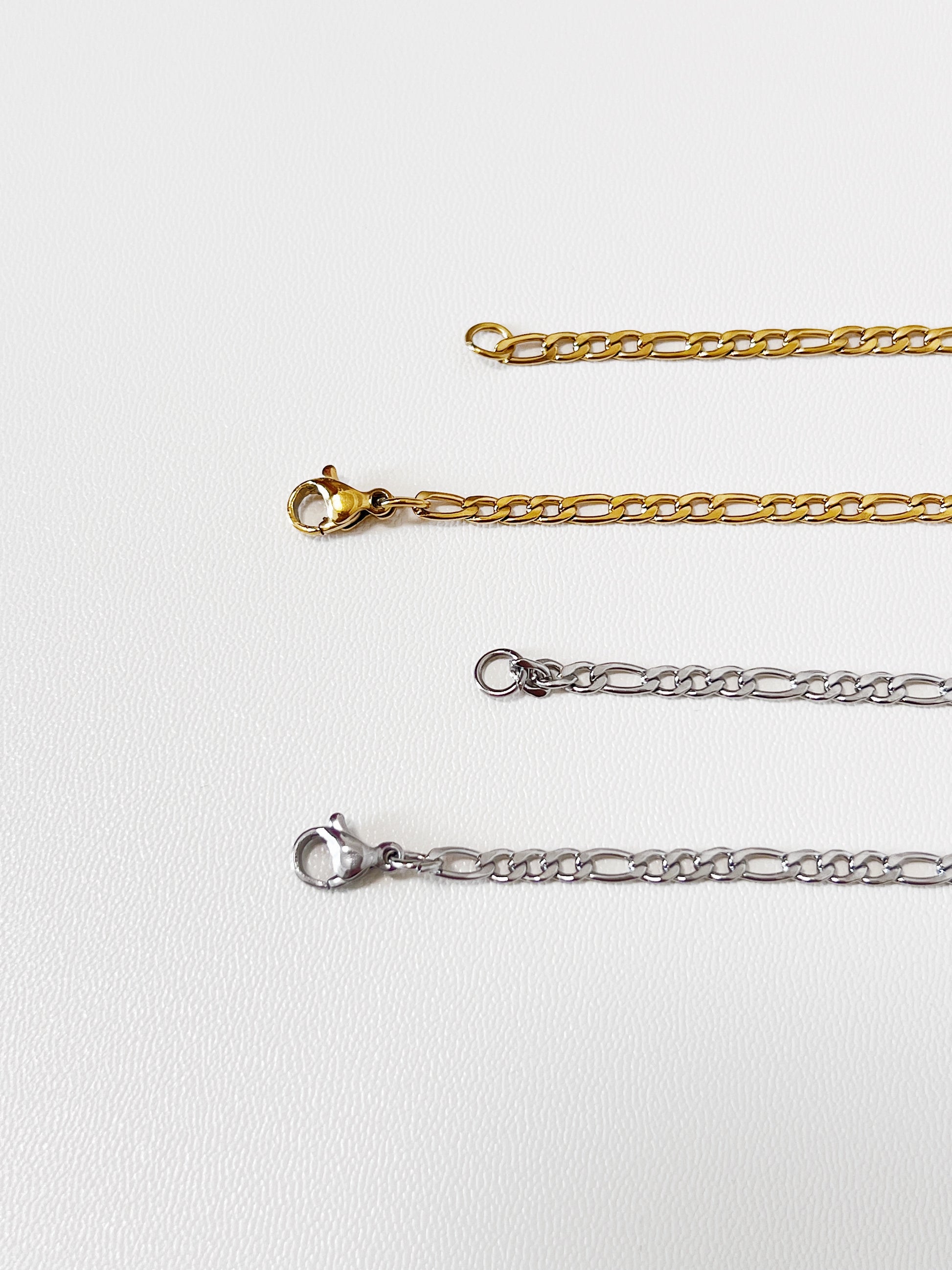 Close-up macro view of the Rhea necklace closure mechanism, focusing on the sleek gold lobster clasp and the clean lines of the silver lobster clasp.