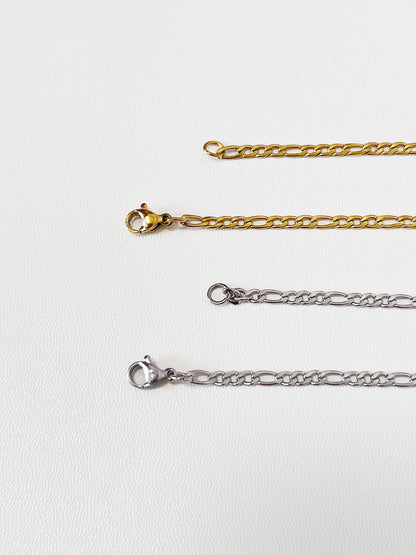 Close-up macro view of the Rhea necklace closure mechanism, focusing on the sleek gold lobster clasp and the clean lines of the silver lobster clasp.