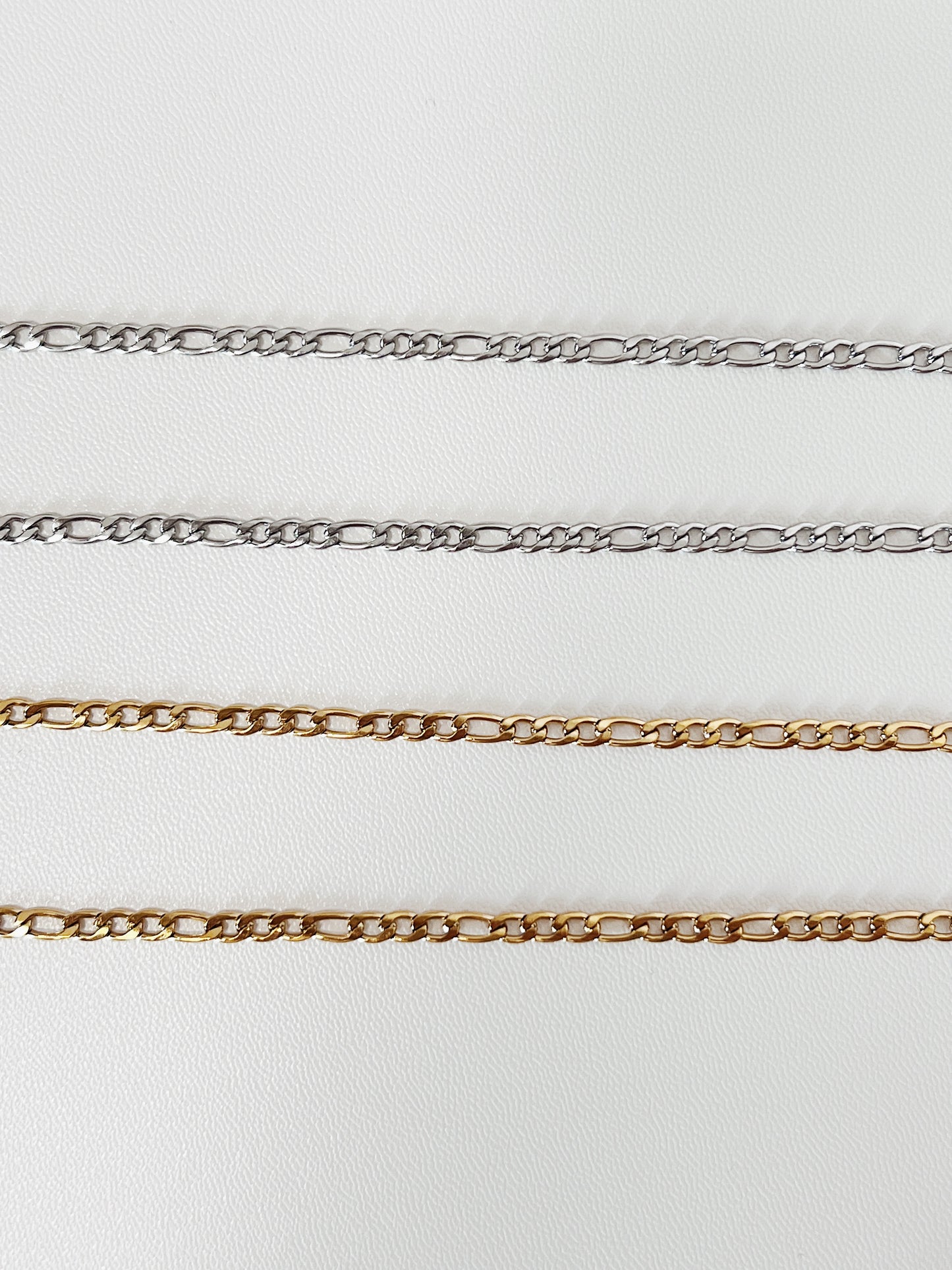 A straight, linear laydown of the gold and silver Rhea Figaro chain, emphasizing the geometric precision and consistent spacing of the Italian link structure.