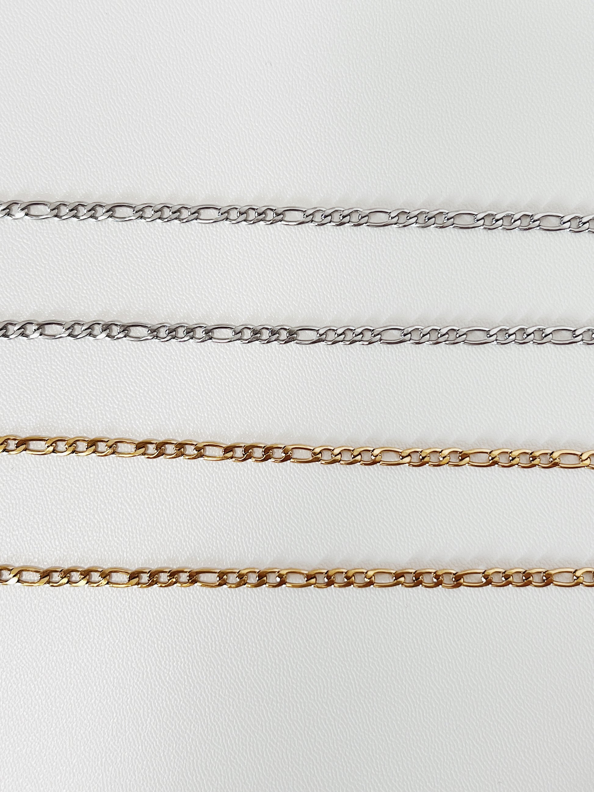 A straight, linear laydown of the gold and silver Rhea Figaro chain, emphasizing the geometric precision and consistent spacing of the Italian link structure.