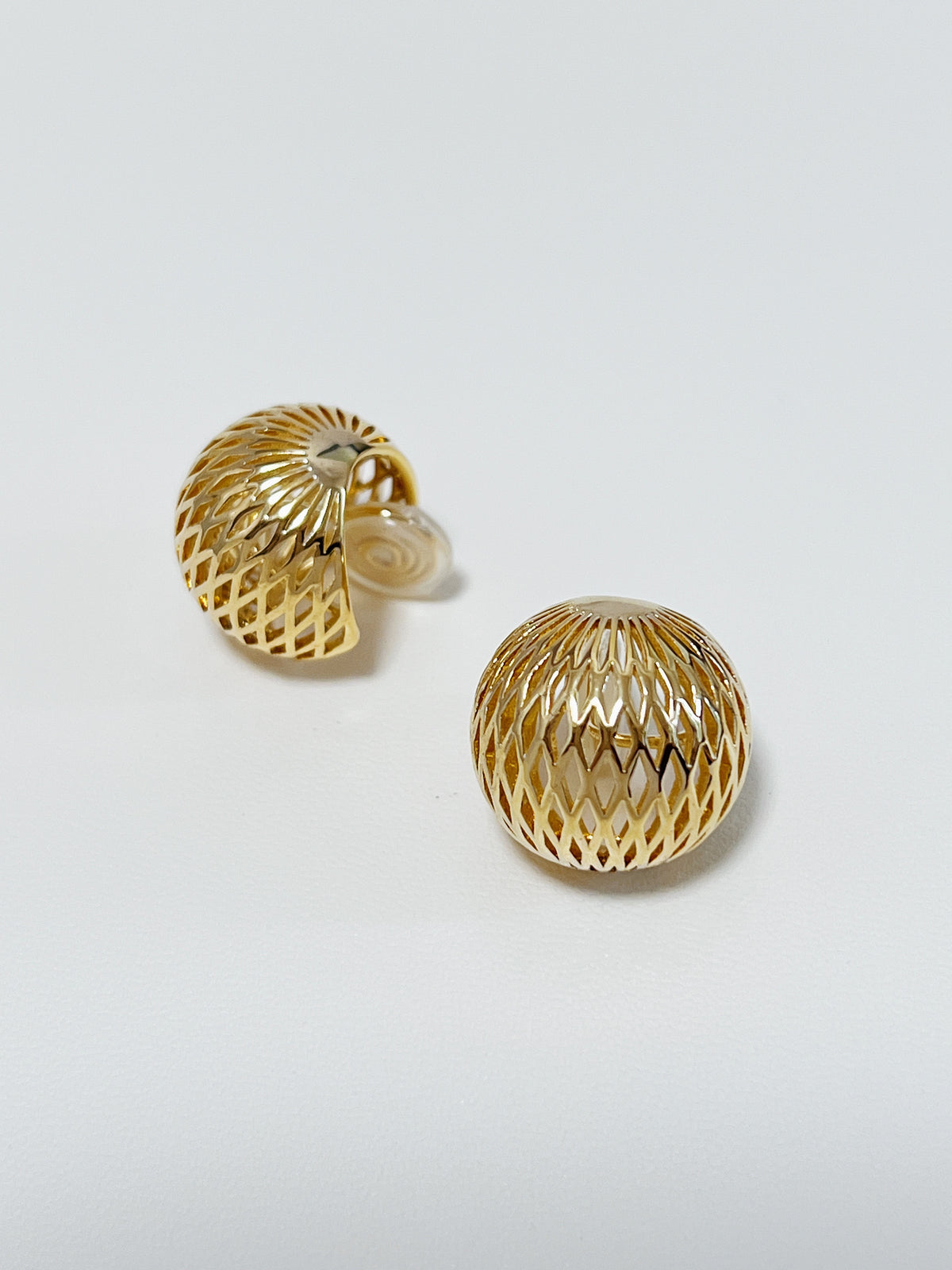 Studio light bouncing off the mirror-polished gold plating of an openwork mesh button clip-on earring.
