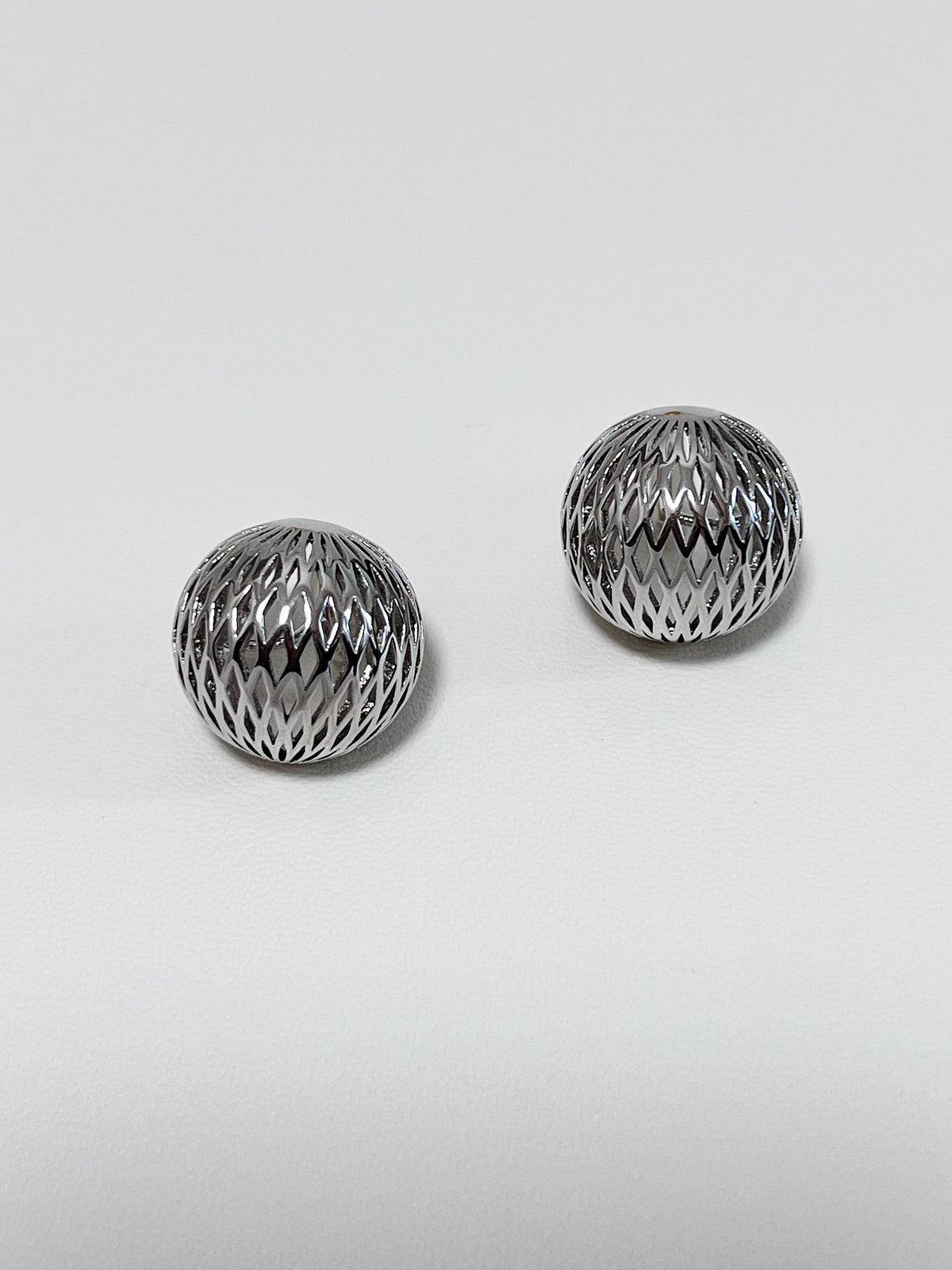 Minimalist flat lay of cool silver openwork clip-on earrings for versatile capsule wardrobe styling.