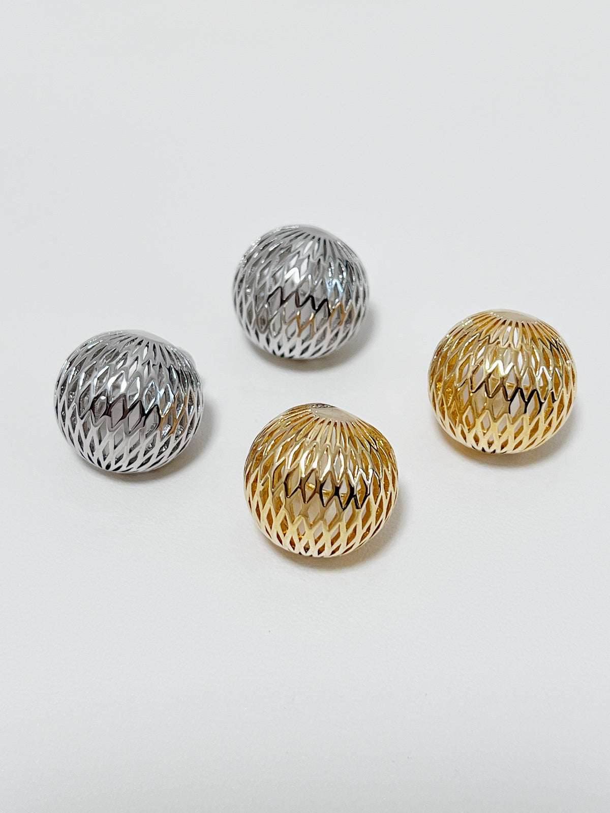 Side-by-side comparison displaying 17mm gold and rhodium silver woven dome clip-on earrings resting in a ceramic dish.