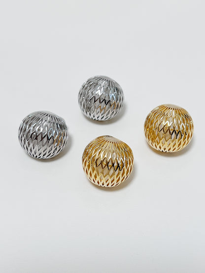 Side-by-side comparison displaying 17mm gold and rhodium silver woven dome clip-on earrings resting in a ceramic dish.