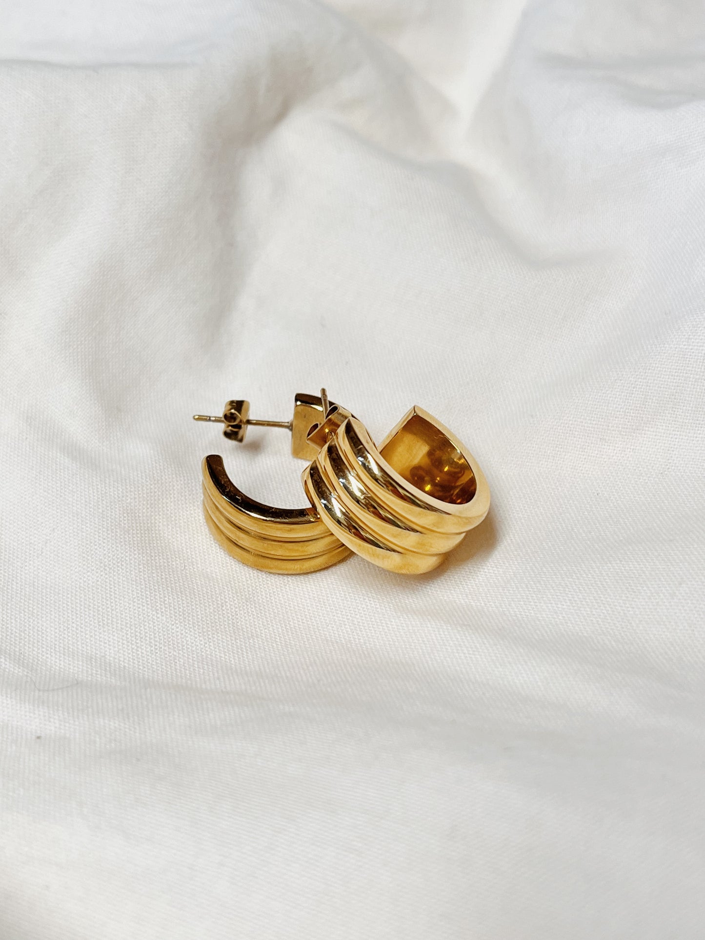 A flat lay displaying the intricate triple-ridge architecture of the premium Lucia gold hoops, highlighting the secure post-and-butterfly closure.