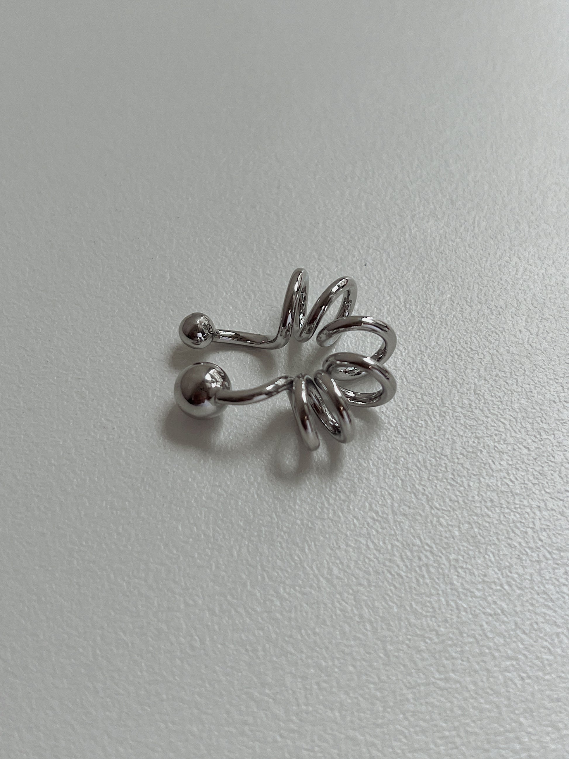 Silver Lis Swirl Ear Cuff on a minimalist, light-grey textured background.