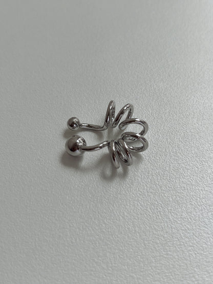 Silver Lis Swirl Ear Cuff on a minimalist, light-grey textured background.