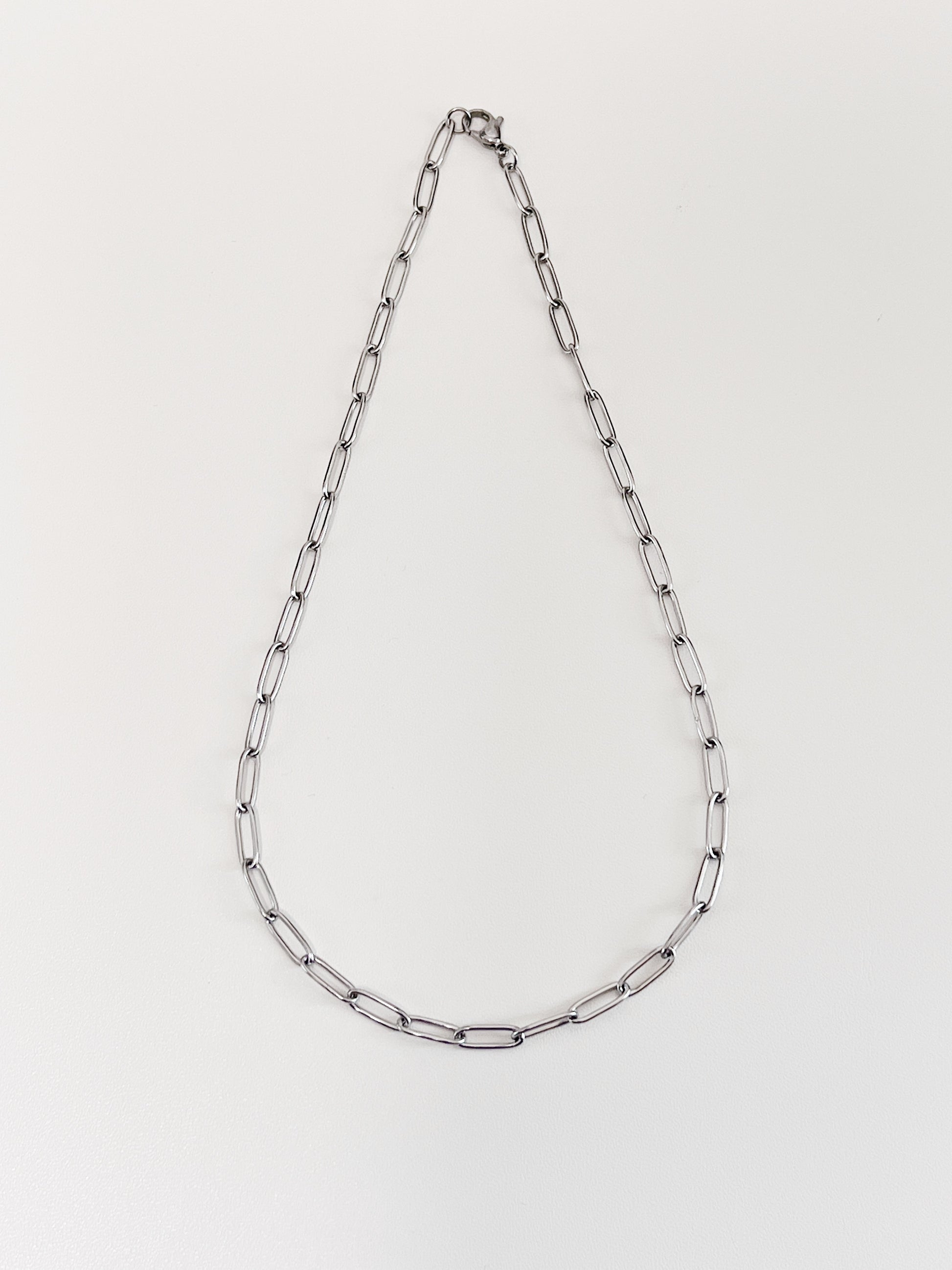 The 4mm thick silver paperclip link necklet laid out symmetrically to display its airy minimalist structural framework
