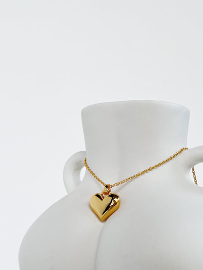The volumetric solid gold Lia heart necklace draped elegantly over a minimalist white ceramic female body-sculpture vase to highlight its three-dimensional curves