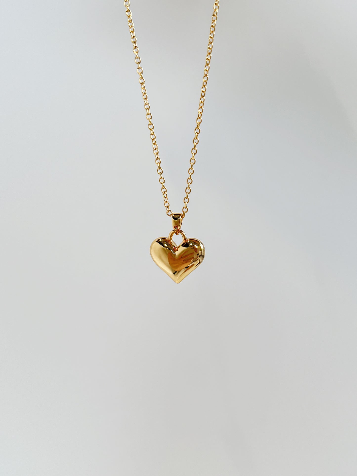 A close-up product perspective highlighting the smooth mirror-polished facets and thick top bale of a solid gold puffy heart charm