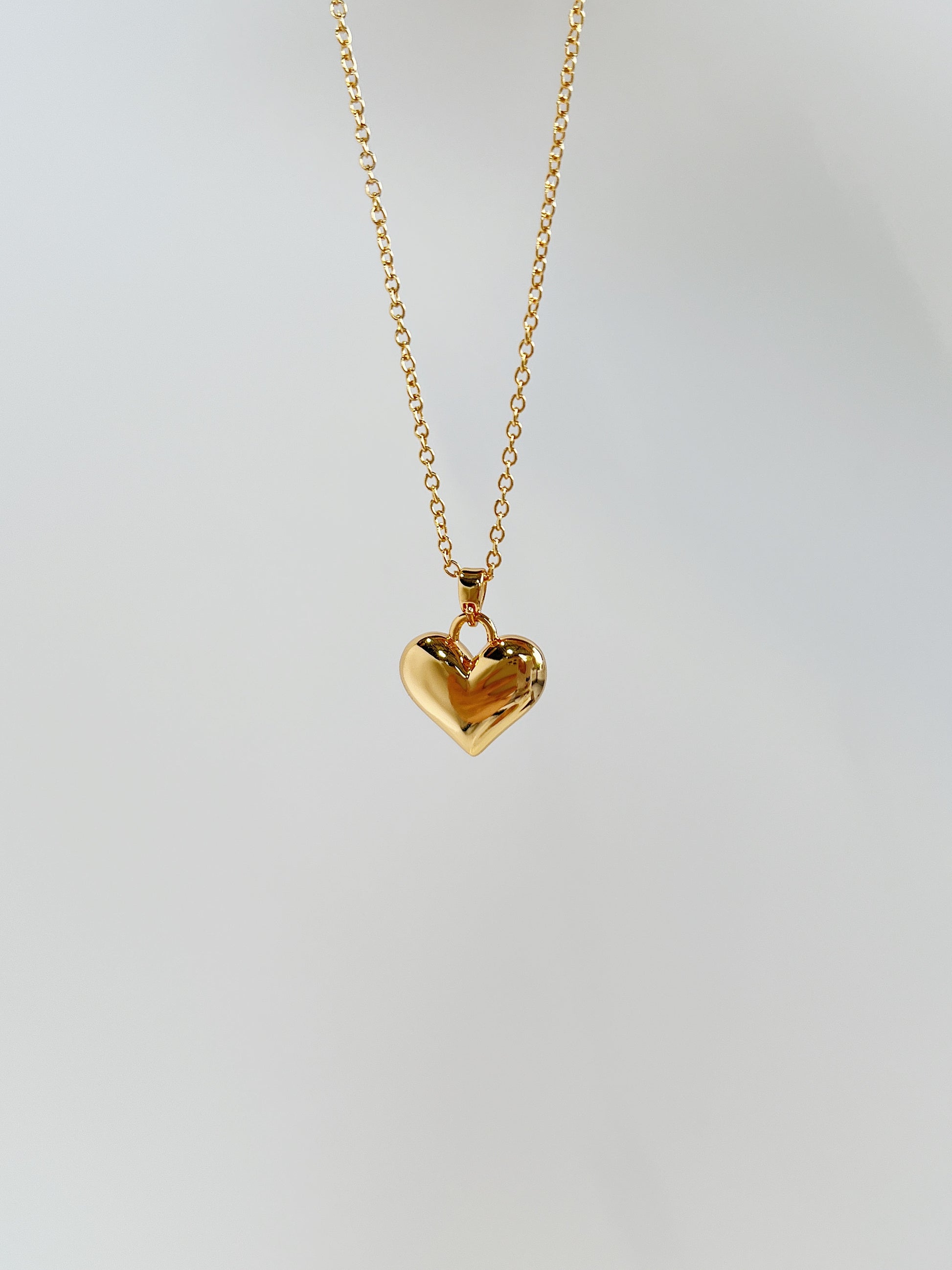 A close-up product perspective highlighting the smooth mirror-polished facets and thick top bale of a solid gold puffy heart charm
