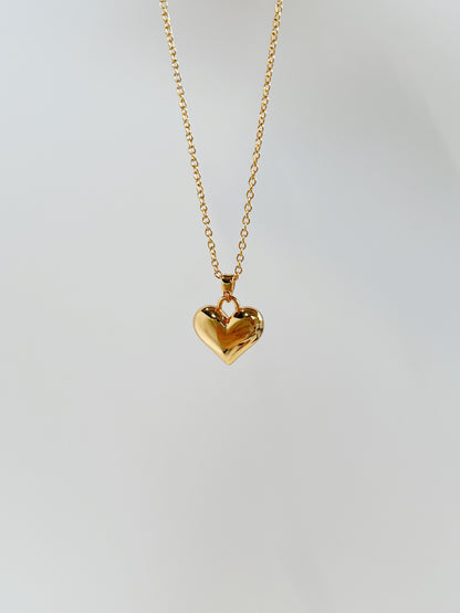 A close-up product perspective highlighting the smooth mirror-polished facets and thick top bale of a solid gold puffy heart charm