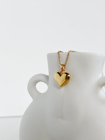 A precise catalog presentation of the 18k gold PVD puffy heart necklace resting gracefully on an aesthetic white ceramic sculpture