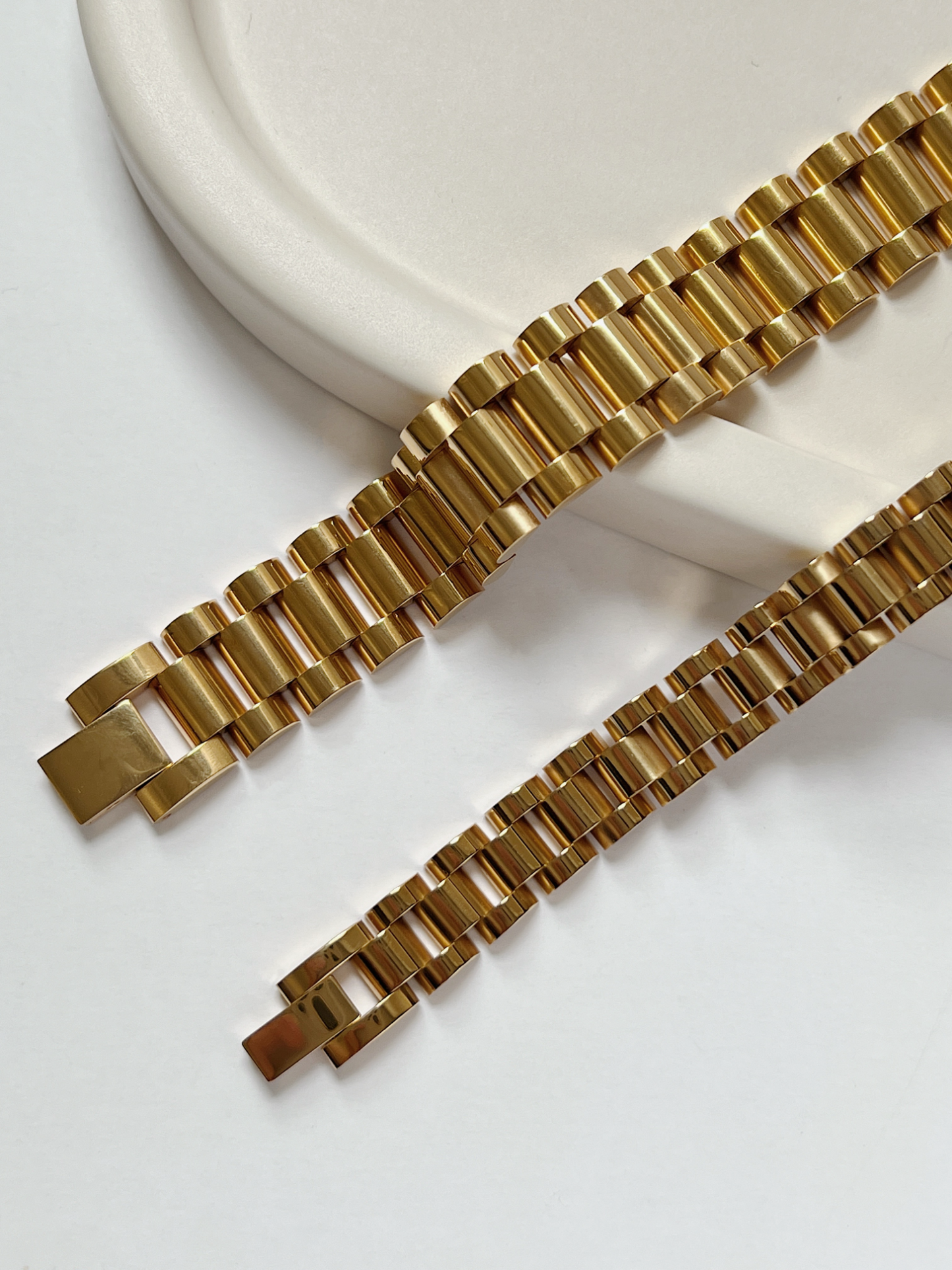 Flatlay view comparing 10mm and 15mm Spencer watch band bracelets in 18K gold finish on neutral stone surface.