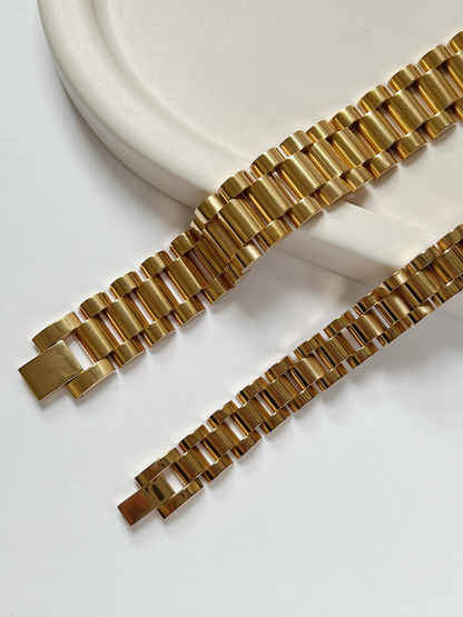 Flatlay view comparing 10mm and 15mm Spencer watch band bracelets in 18K gold finish on neutral stone surface.
