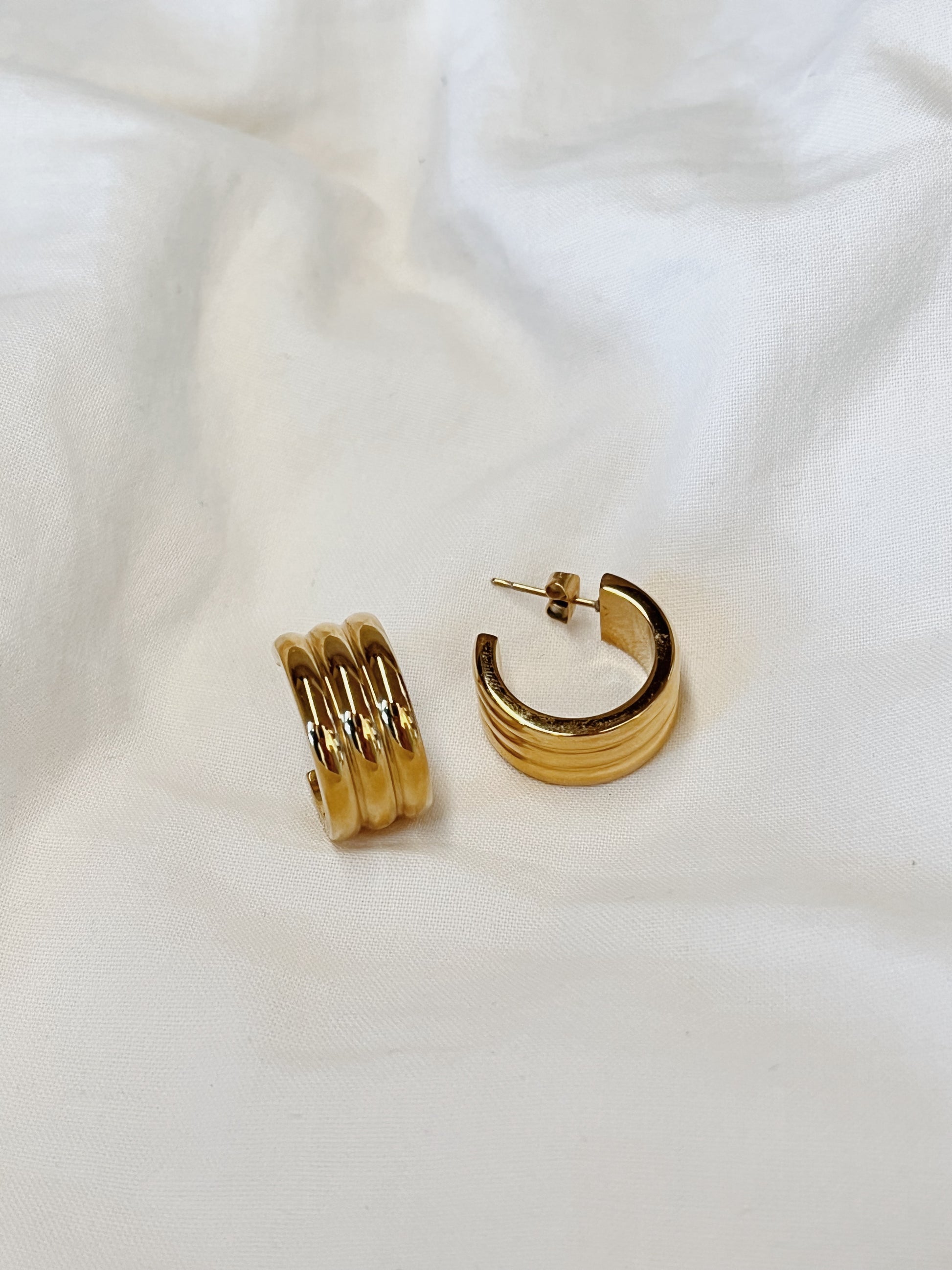 Studio product photograph focusing on the heavy-gold texture and sculptural grooves of the Lucia statement hoop earring.