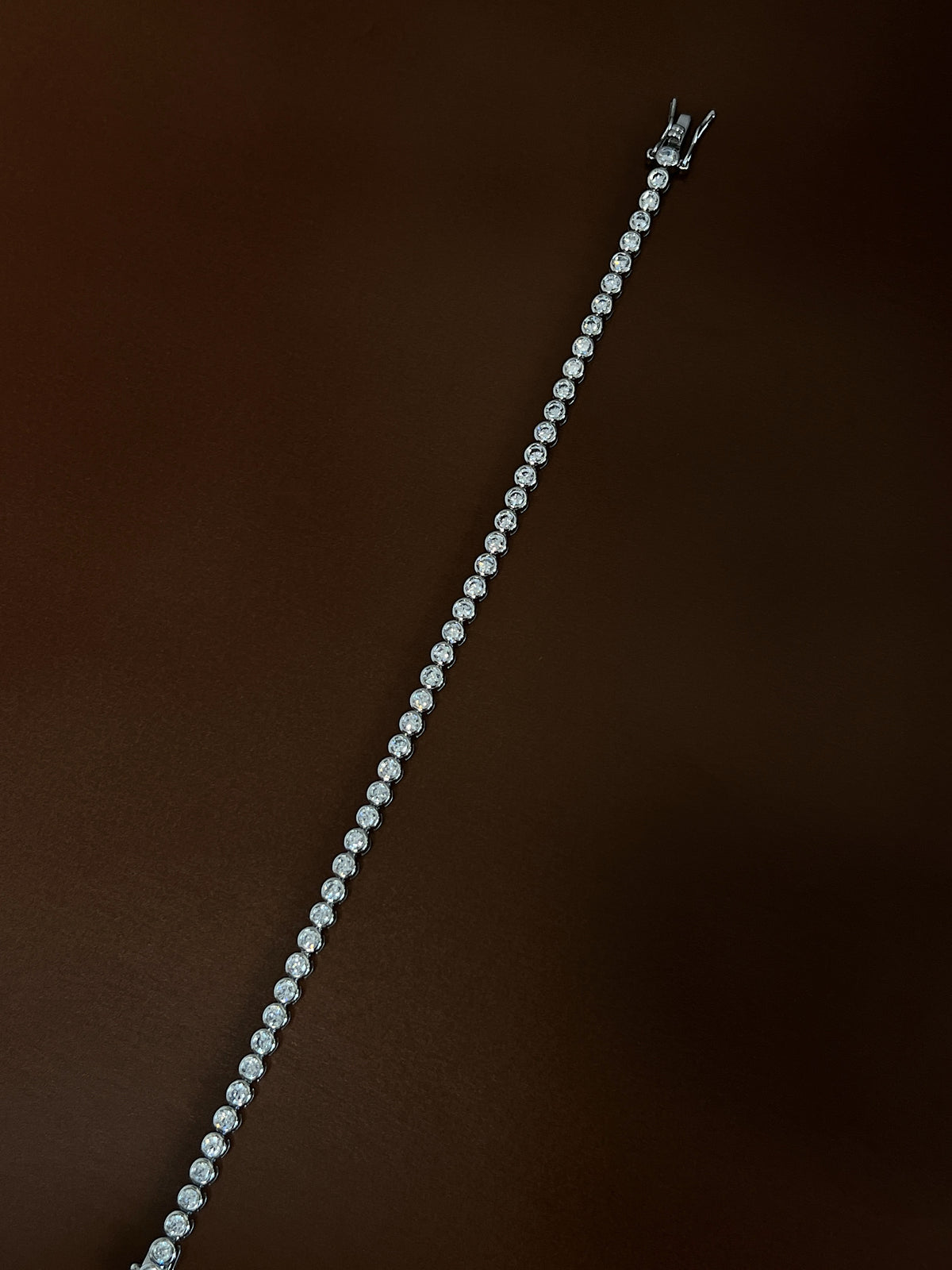 Overhead diagonal angle highlighting the high-luster rhodium finish and luminous 3mm bezel-set stones on a dark background.