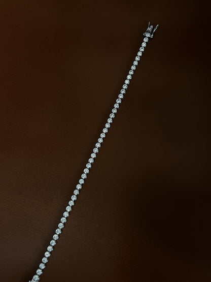 Overhead diagonal angle highlighting the high-luster rhodium finish and luminous 3mm bezel-set stones on a dark background.