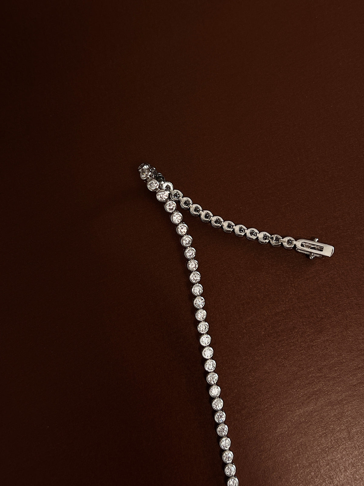 Close-up view of the double-latch box clasp closure and smooth bezel stone settings of a rhodium silver tennis bracelet.