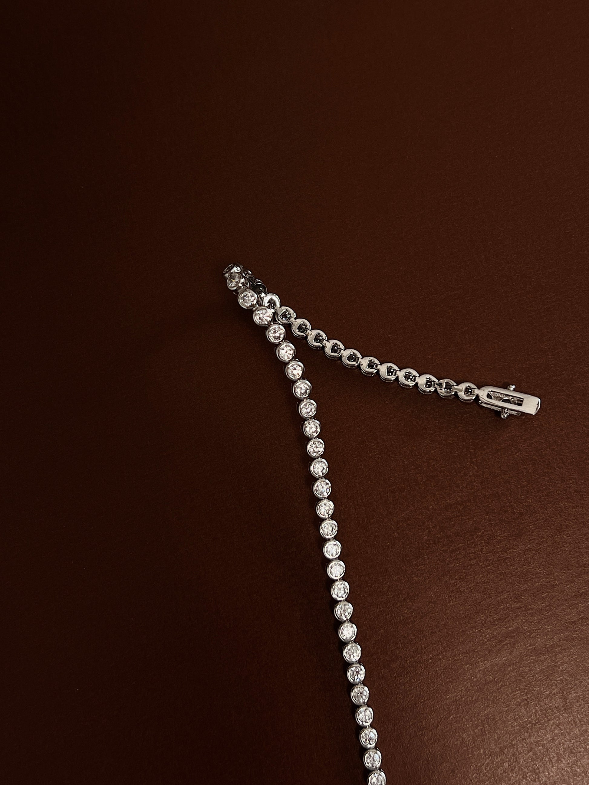 Close-up view of the double-latch box clasp closure and smooth bezel stone settings of a rhodium silver tennis bracelet.