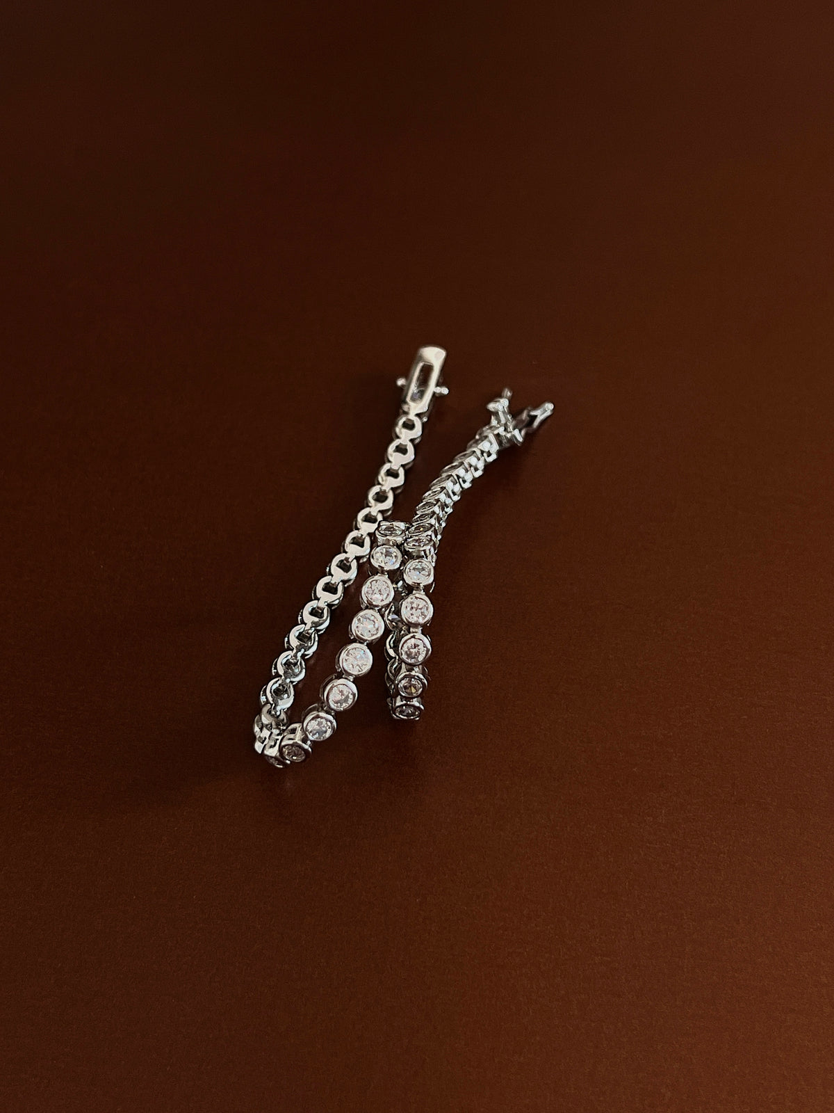 Silver bezel-set tennis bracelet looped gracefully on a dark brown surface highlighting its soft, articulated link structure.