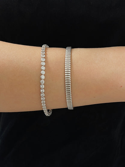 Horizontal wrist view showing the smooth, flush bezel-set stones of a silver tennis bracelet paired with a textured metallic cuff.